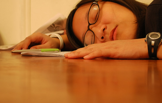 This is an image a woman at work asleep with her head on the desk, appearing exhausted from her work schedule.
