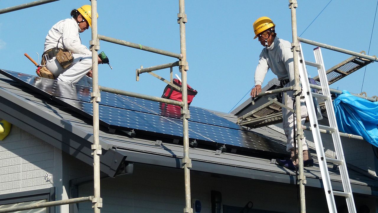 This is an image of two workers in protective gear on a rooftop. They are installing solar panels.