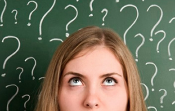 This is an image of a woman&rsquo;s face from her nose up, with her eyes looking upward. Behind her is a chalkboard filled with different sized question marks.