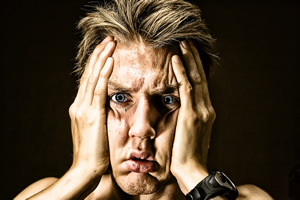 This is an image of man&rsquo;s face with his hands clasping both sides. He appears very overwhelmed.