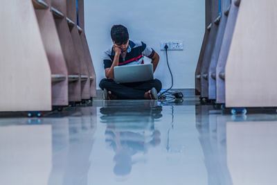 This is an image of a single male teen in a hallway, staring at his computer.