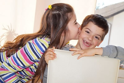 This image is of a a girl, with long brown hair, leaning in to kiss a younger, toothless boy.
