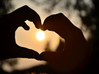 This is an image of two hands, making a heart shape, with the sun setting in the background.