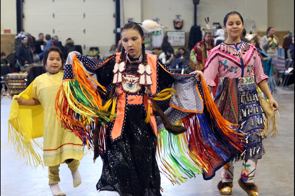This image is of three girls dressed in traditional attire dancing at a pow wow.