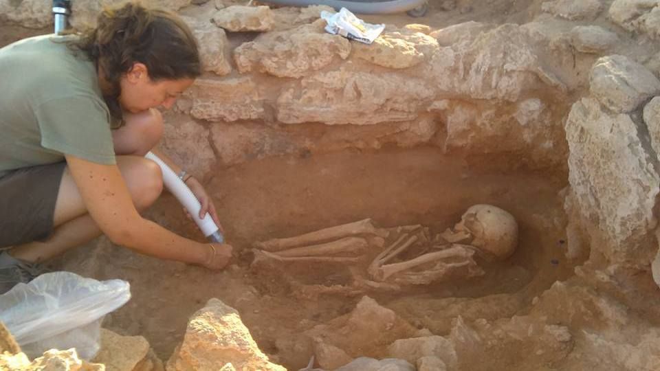 This image shows a woman carefully dusting away sand from a half buried skeleton.