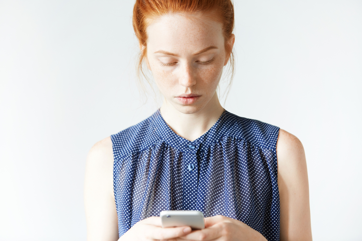 This is an image of a young, redheaded woman who is inputting data into her cell phone.