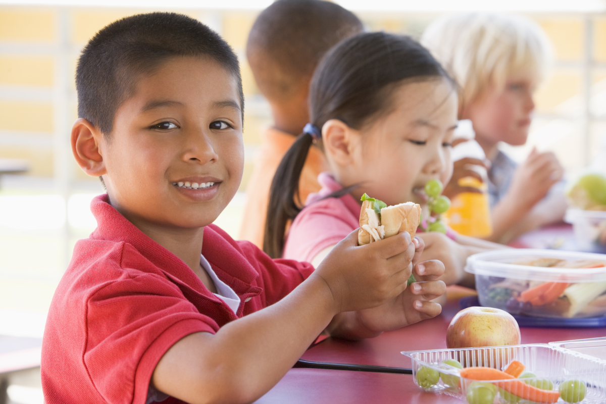 This image is of a group of young children eating a free breakfast at the school cafeteria table.