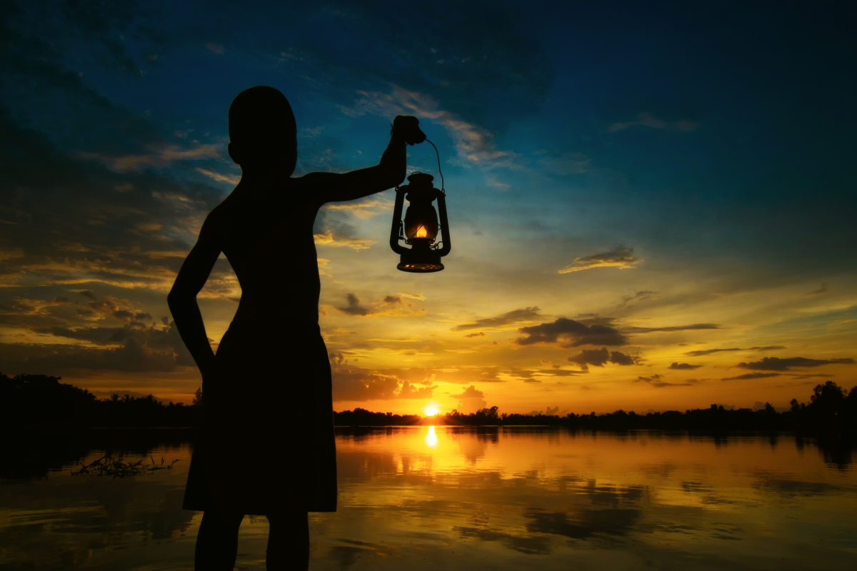 This is an image of a child holding a storm lantern while watching the sunset.