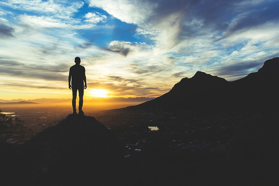 This is an image of a person who is standing at the edge of a cliff while watching the sun set in the distance.