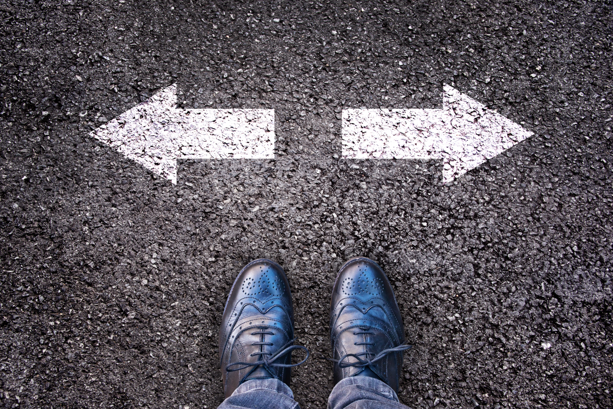 This is an image of someone standing behind two arrows which are pointing in the exact opposite direction to each other.