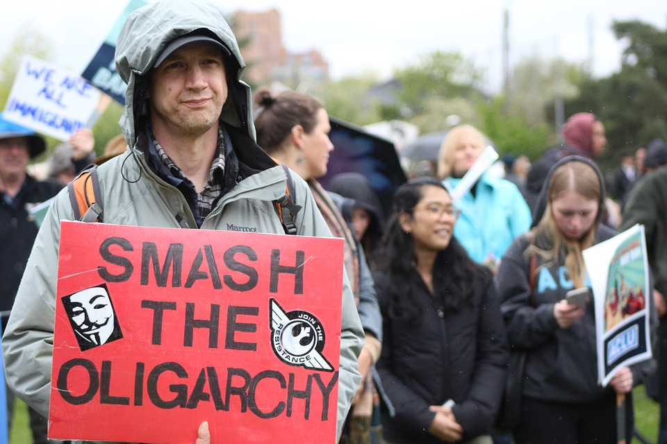 This is an image of a crowd of protesters. One man close to the camera wears a sign that reads, “smash the oligarchy.”