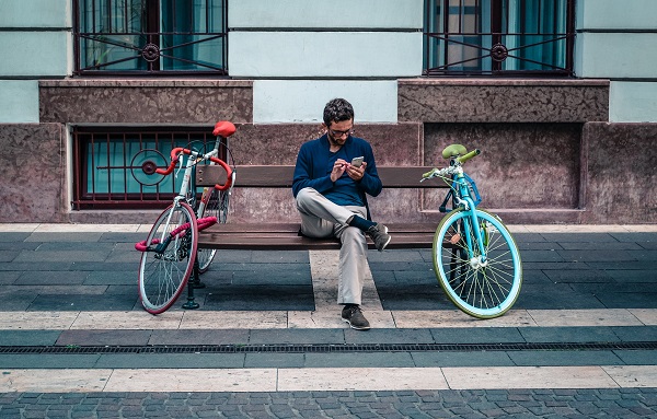 This is an image of a man sitting on a bench using software on his smartphone.