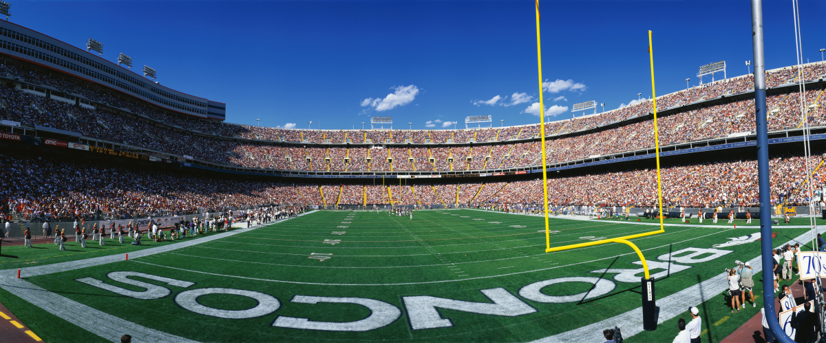 This is an image of the field at the Denver Broncos stadium from behind the end-zone.  There are fans in the stadium and the game is in progress.