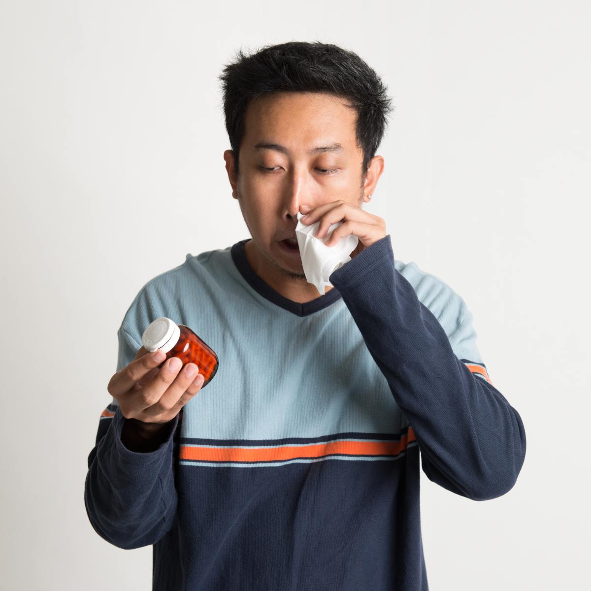 This is an image of a man wiping his nose while looking at a bottle of medication.