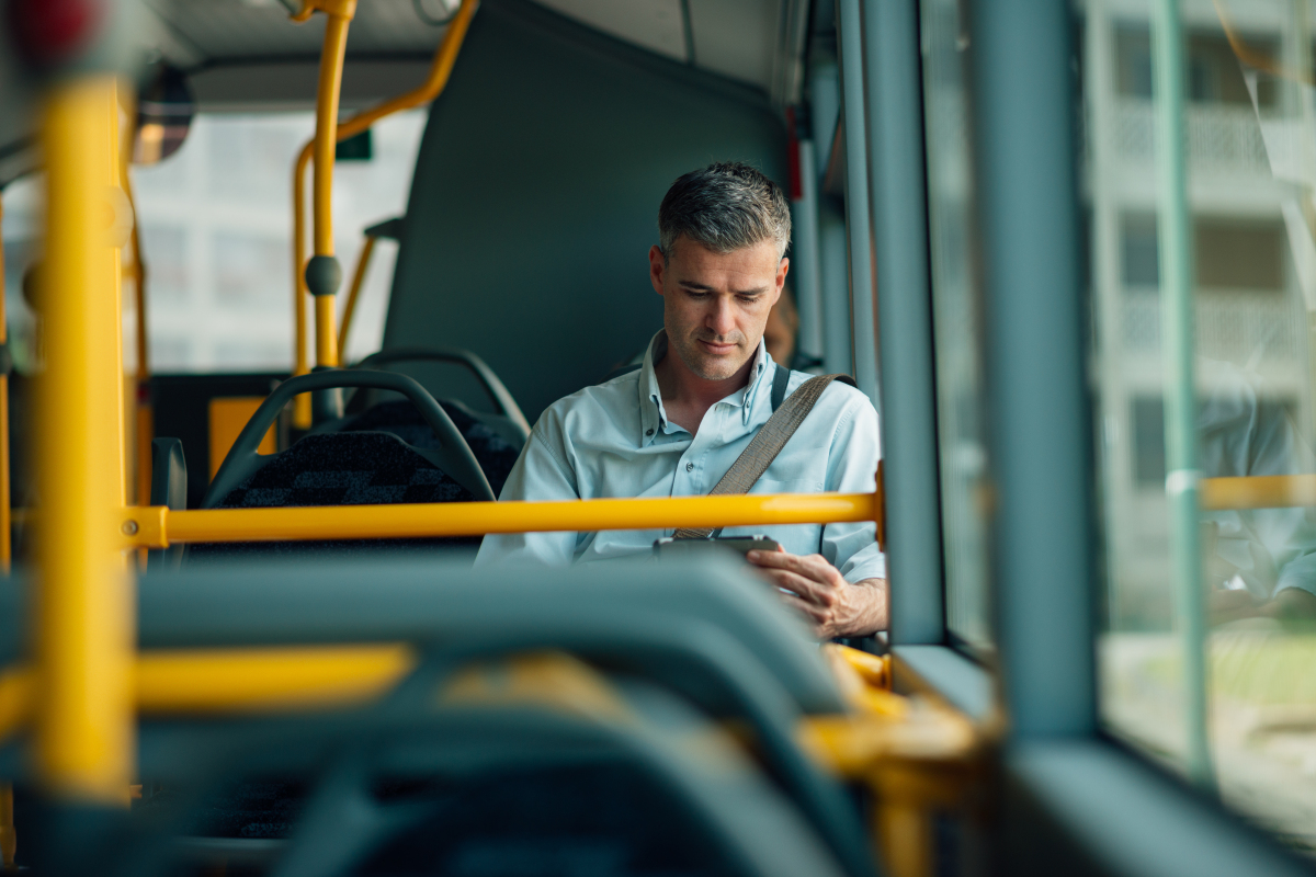 This is an image of a man on a bus looking down at his tablet.