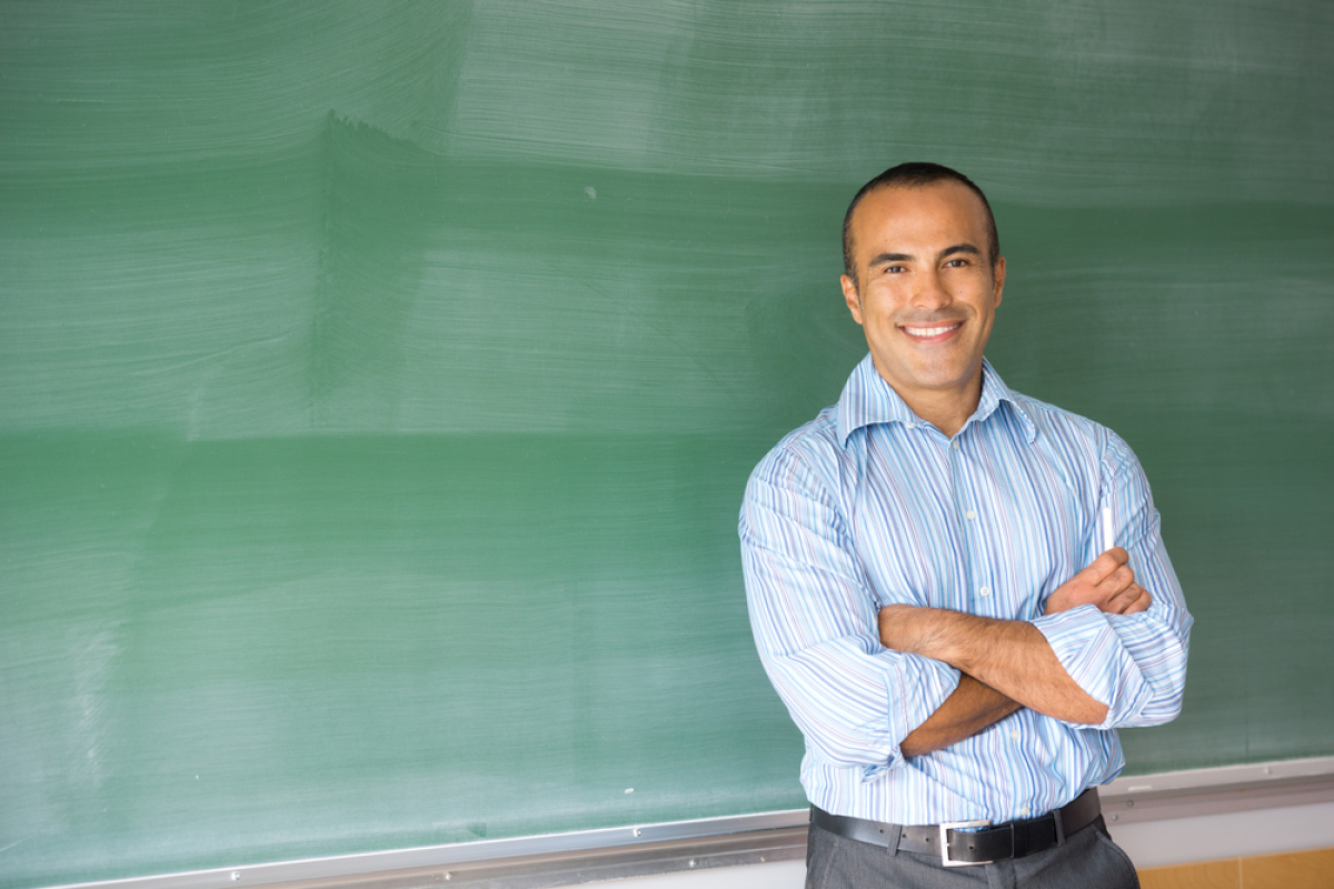 This is an image of a teacher standing in front of a green chalk board.