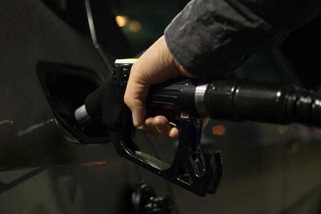 This is an image of man's hand holding a fuel nozzle while refueling a car.