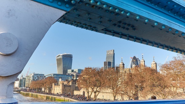 An image of London England's skyline taken from under a bridge. The buildings have various shapes including cylinders, squares and rectangles.