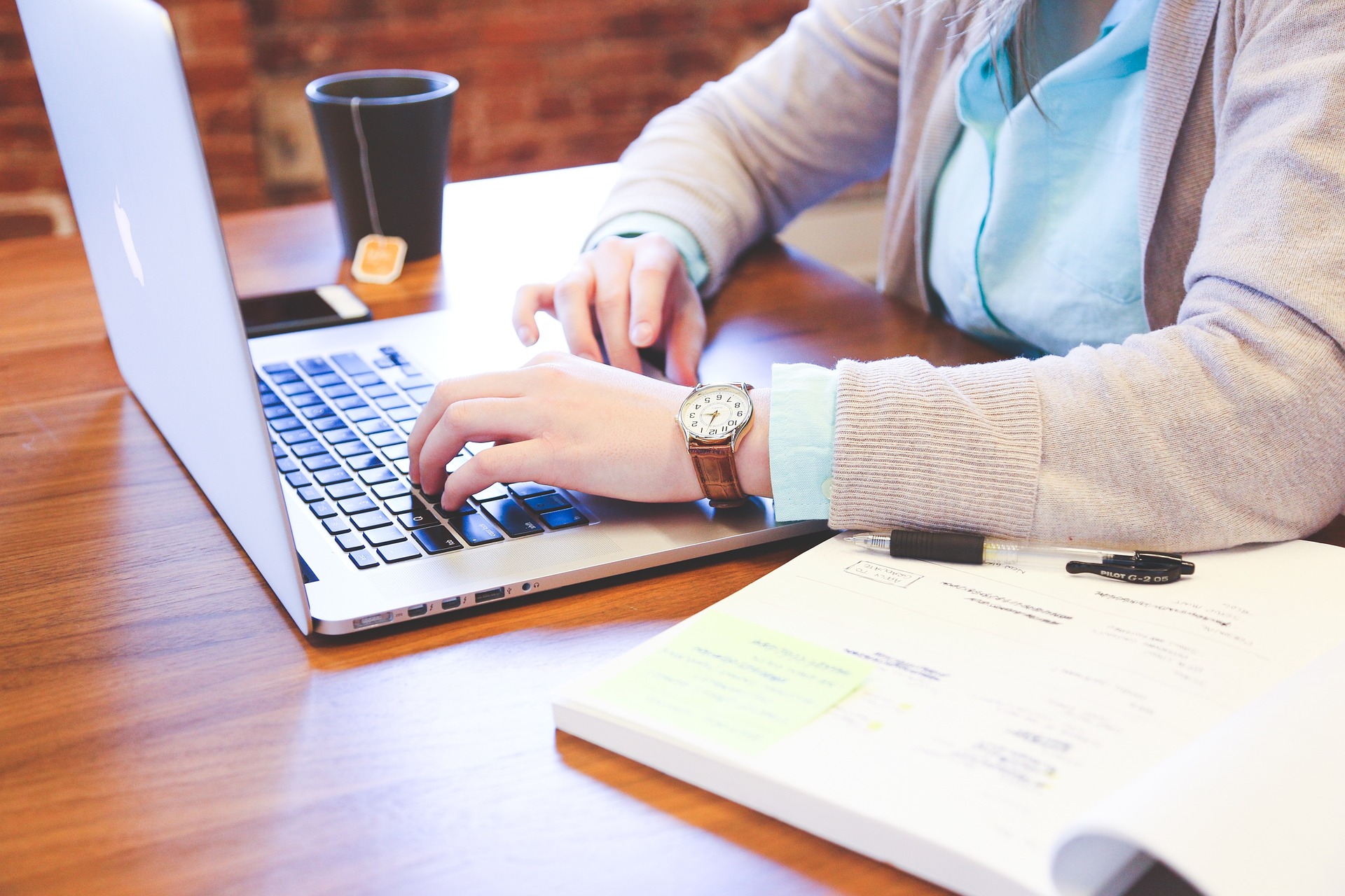 An image of a woman working at a computer with a financial notebook open. She seems to be entering values in order to create a budget or complete her taxes.