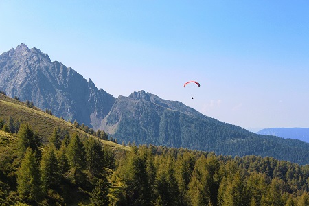 An image of an individual paragliding over a forest and mountains.