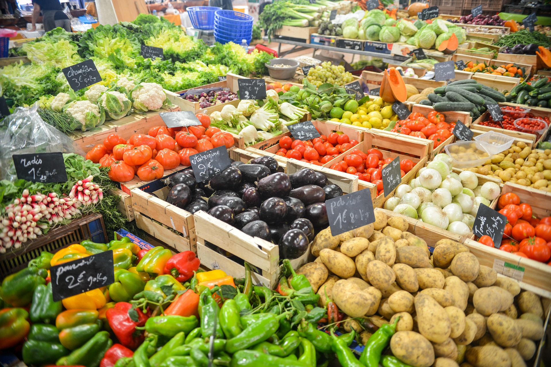 This is an image of a market with baskets of fresh produce as far as the eye can see. The baskets contain red and green peppers, potatoes, eggplants, onions, tomatoes, radishes, cucumbers, and a number of lettuce varieties. Each type of produce is in its own area, making it easy to see what is available.