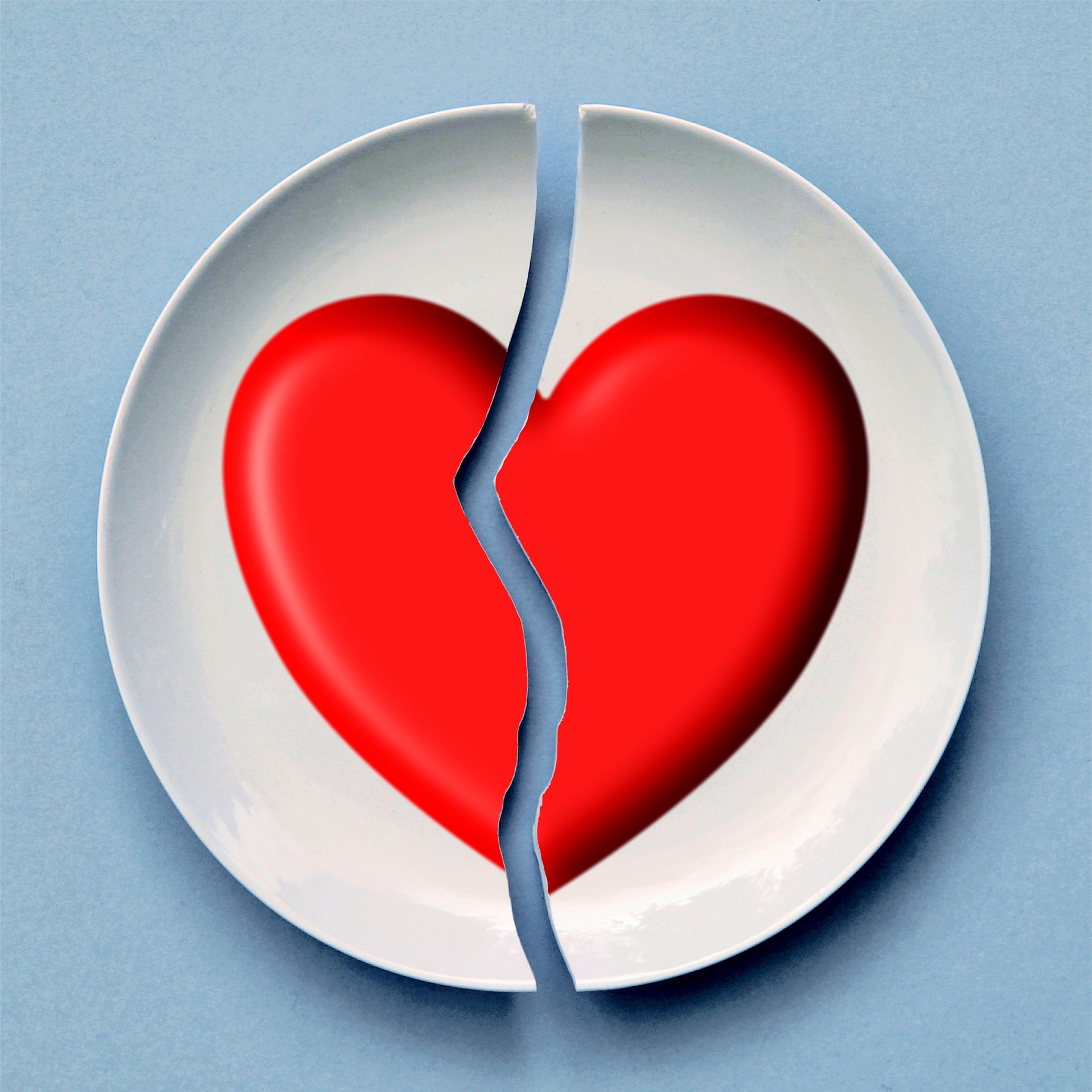 This in an image of a white plate on a blue background. The plate has a classic red heart on it, and the plate is broken into two pieces down the centre and through the heart.