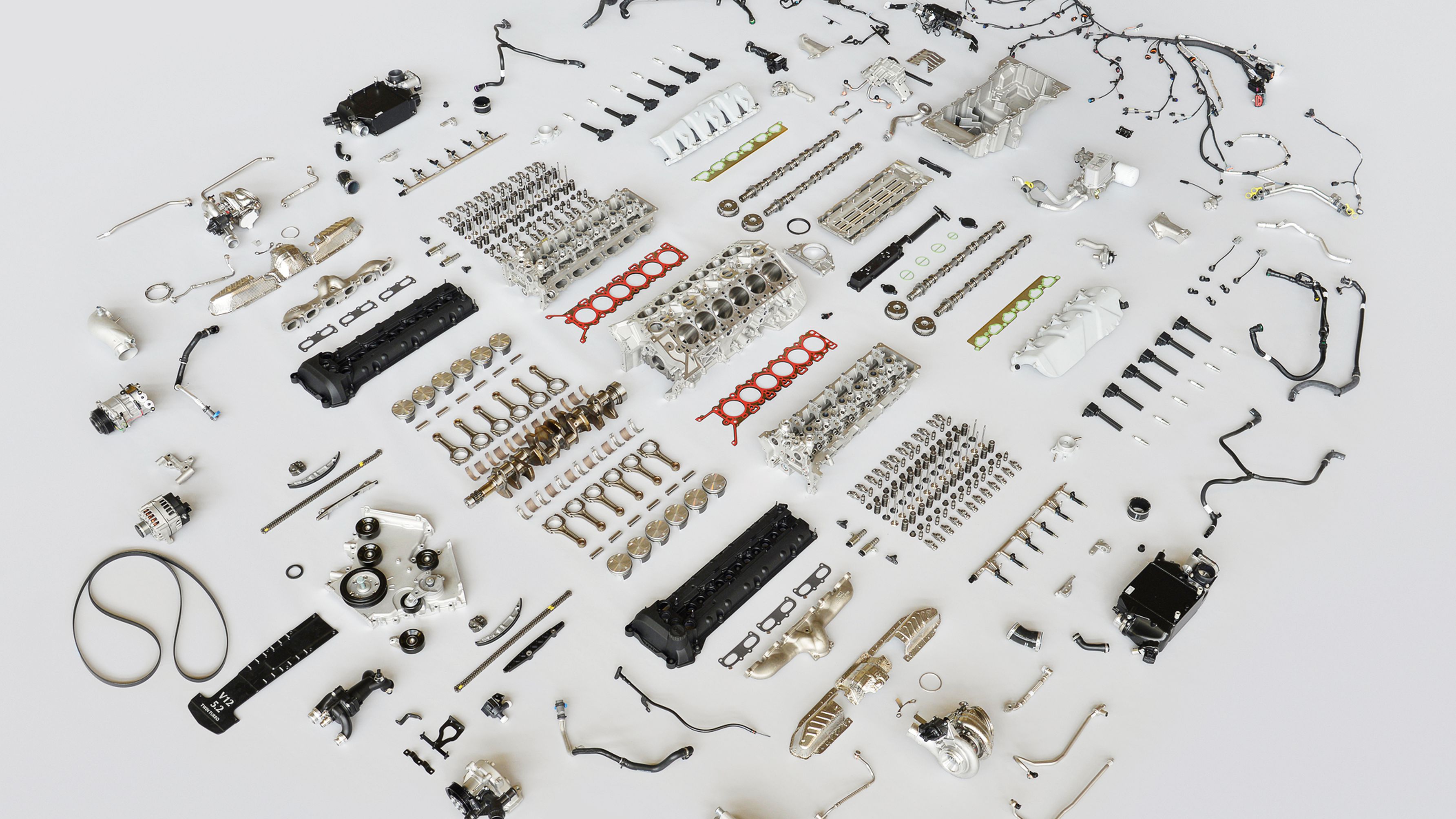 This is an image of an engine that has been broken down into all its component parts on a grey surface. Hundreds of small mechanical parts are displayed neatly.