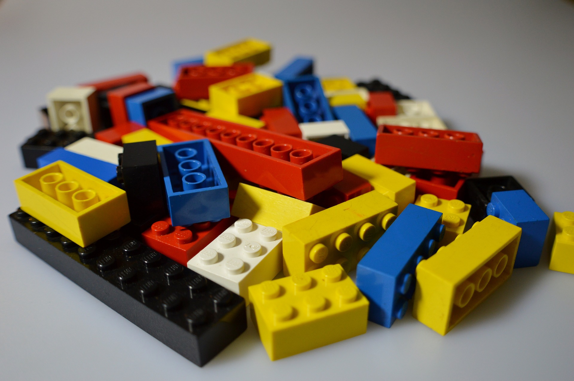 This is an image of a pile of toy building bricks on a grey surface. There bricks are a variety of different lengths and the colours black, blue, yellow, white, and red.