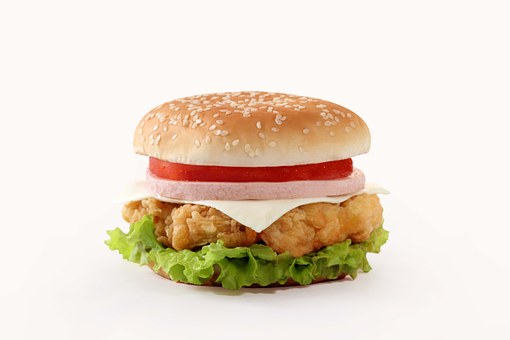 This is a photograph of a chicken burger. The chicken is topped with lettuce, cheese,onion and a tomato all on a sesame seed bun.