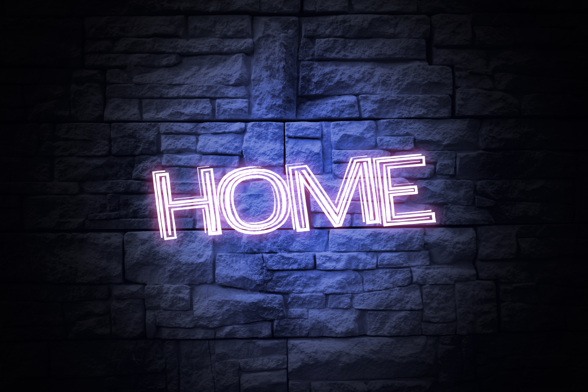This is an image of a neon sign that says HOME and is glowing on top of a brick background.