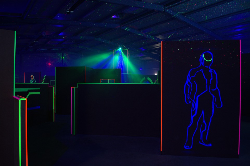 This is an image of a laser tag arena that is mostly dark except for bright fluorescent green, red and blue colours lighting up the obstacles.