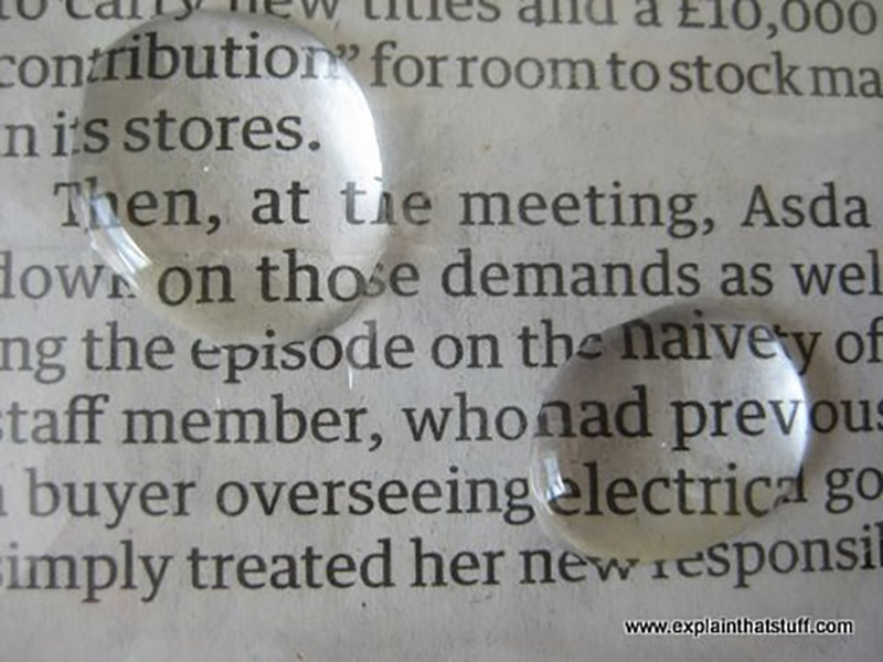 This is an image of two water droplets on a newspaper page. The letters beneath the droplets appear larger than the other letters on the page.