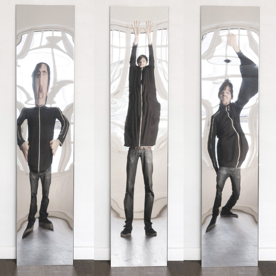 This is an image of three funhouse mirrors showing distorted images of a man wearing jeans and a zipped sweatshirt. The mirror on the left shows the man with a large distorted head and short legs. The centre mirror shows a taller, slimmer man with very short arms extended over his head. The image on the right shows the same man with a distorted midsection and an enlarged arm over his head.