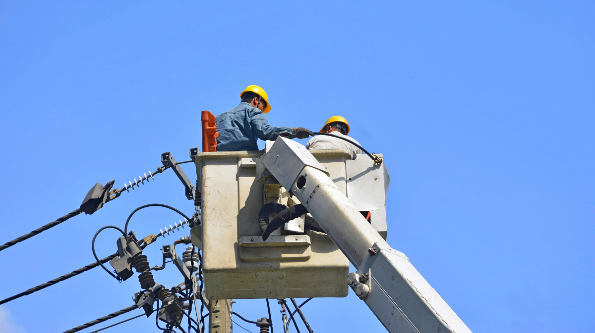 This image depicts two power lineworkers in a hydraulic bucket servicing a transmission line.
