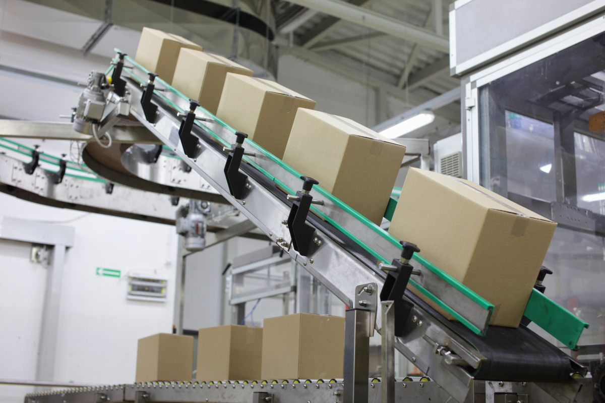 This image depicts a conveyor belt moving five cardboard boxes in a factory setting.