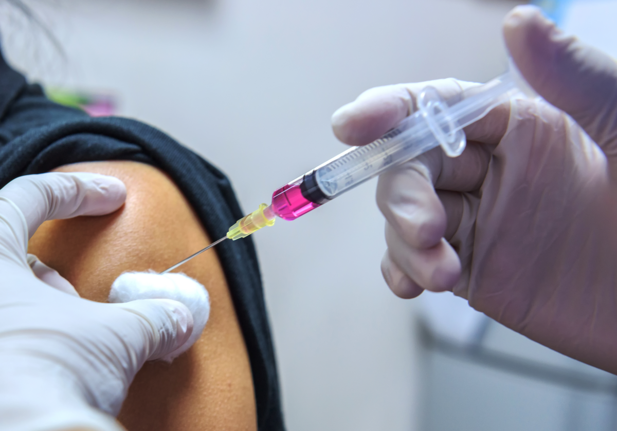 This close-up image depicts a nurse using a syringe to inject a patient with vaccine. 