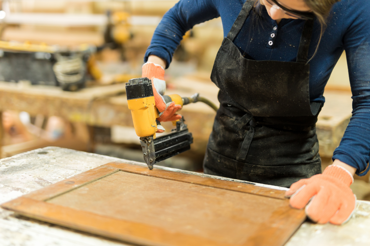 This image depicts a worker using an air powered nail gun to assemble a cabinet door.
