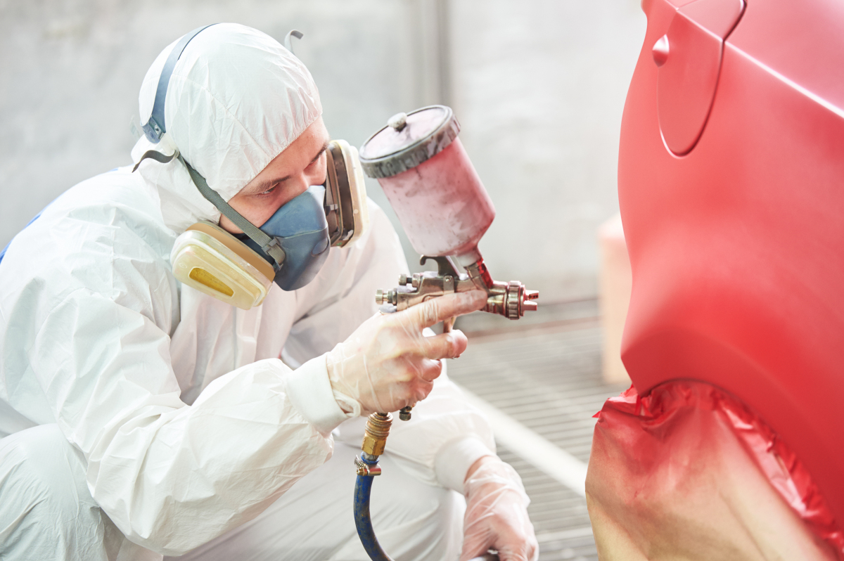 This image depicts a worker spraying paint onto a car.