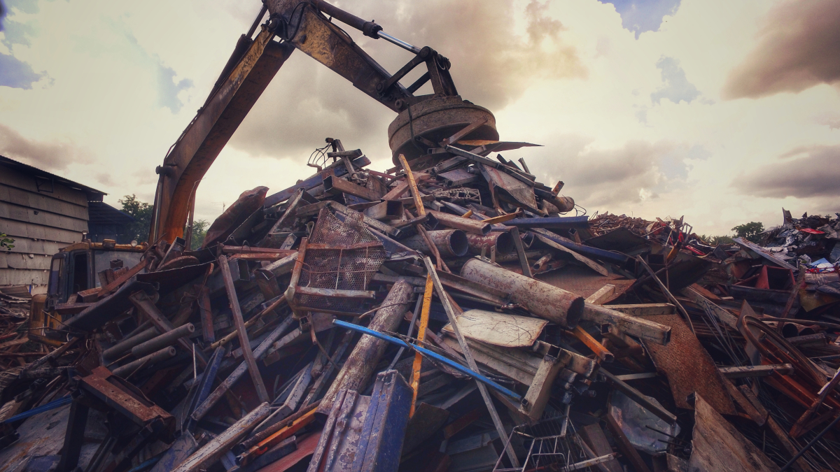 This image depicts a backhoe with an electromagnetic attachment picking up metal at a recycling facility. 